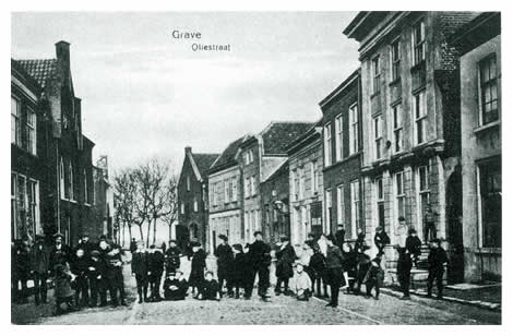 De Markt weer overstekend, komen we door het Korte Rogstraatje in de Oliestraat met uitzicht op de bomen van de Maaskade. Links staat de voormalige synagoge, die nu in gebruik is als Gereformeerde Kerk. Het pakhuis op de achtergrond is de brouwerij van Van Alderwaereldt, die in 1915 geheel uitbrandde. Rechts zien we een leuk poortje, dat toegang geeft tot het straatje van de vroegere Pauselijke Staat bij de Oude Haven.